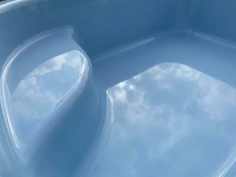 Close-up of a glossy light blue fiberglass pool surface and molded step